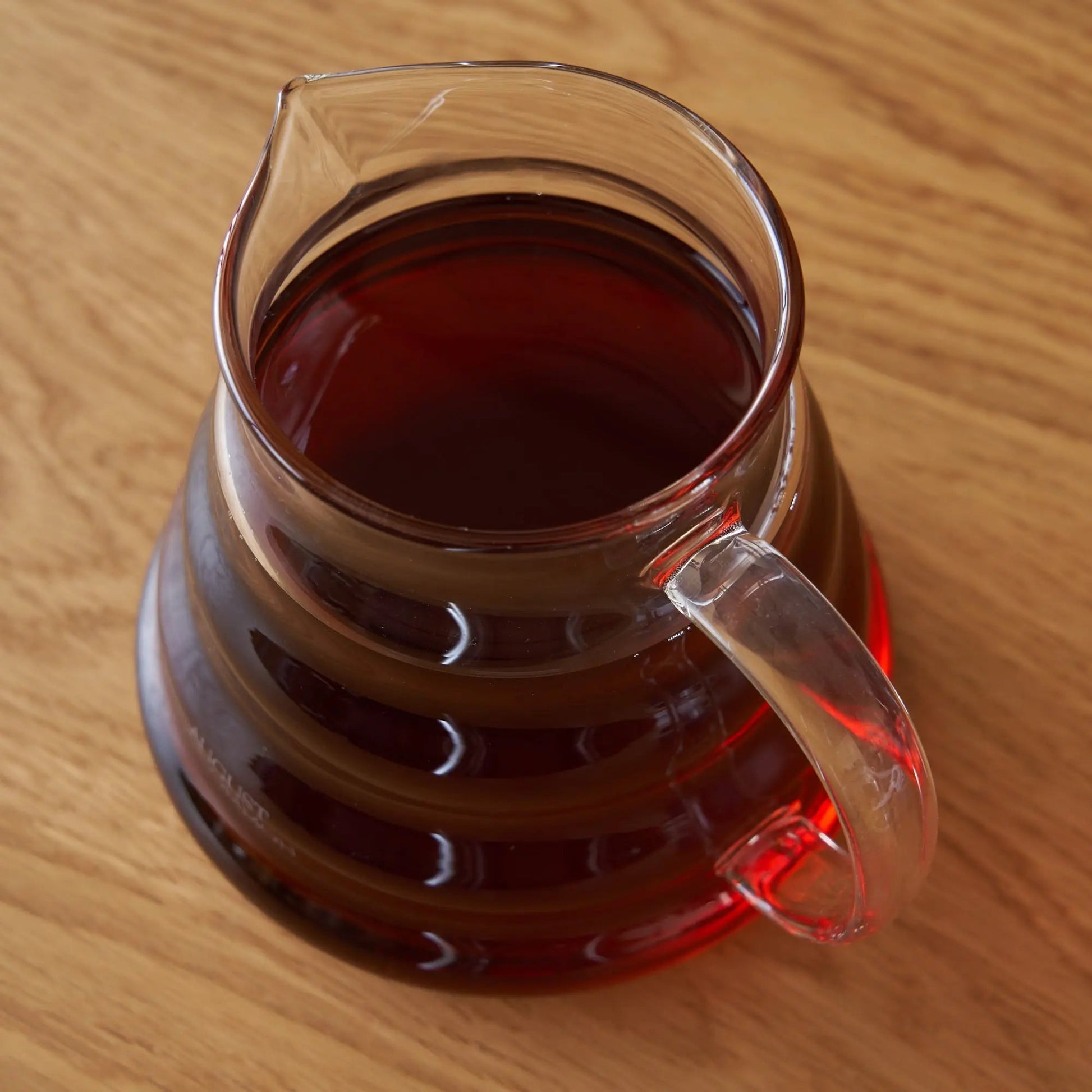 Two-cup glass teapot with handle, amber tea visible from above on wood.