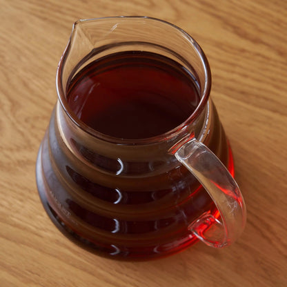 Two-cup glass teapot with handle, amber tea visible from above on wood.