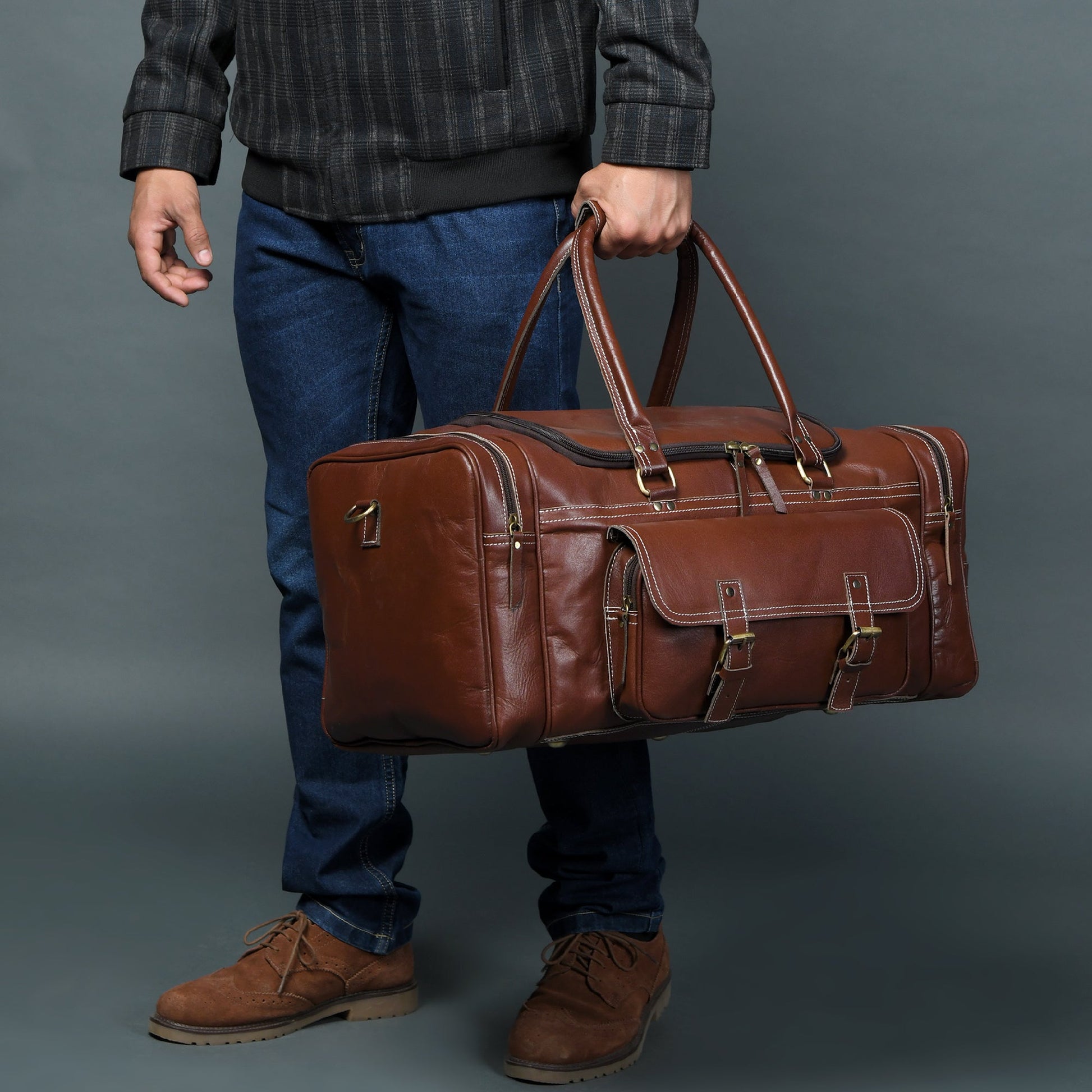 Brown leather weekender duffel being carried with dual handles and adjustable crossbody strap