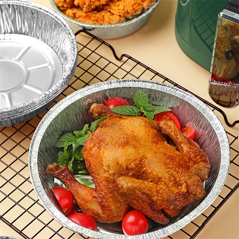 Round aluminum foil liner pan filled with roasted chicken and tomatoes on wire rack
