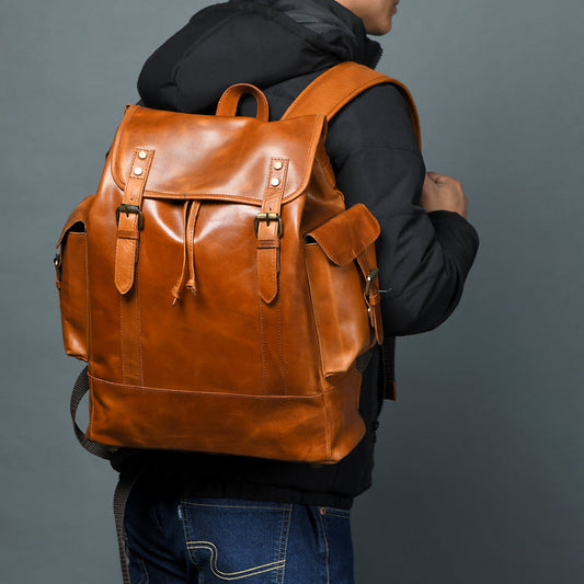 Brown leather laptop backpack with front flap, buckled straps, and top handles.