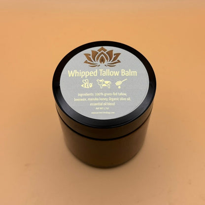 Tallow balm jar with black lid and blue label reading “Whipped Tallow Balm”