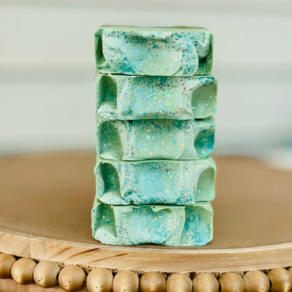 Stack of speckled mint and teal soap bars on a wooden tray
