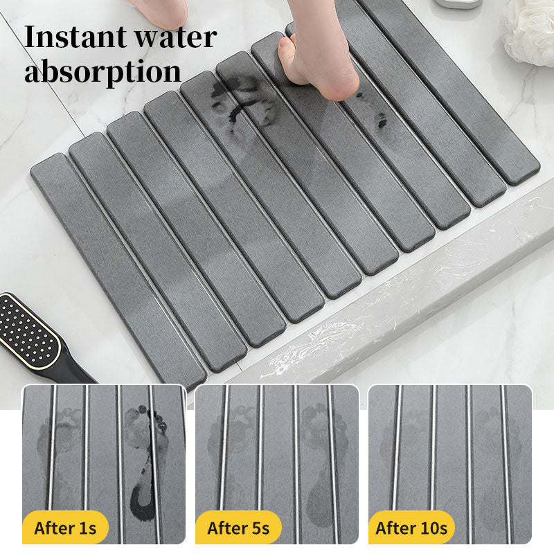 Dark gray diatomite bath mat with raised ribbed tiles and scattered water.