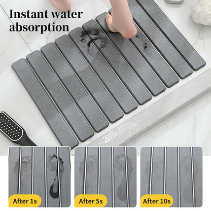 Dark gray diatomite bath mat with raised ribbed tiles and scattered water.