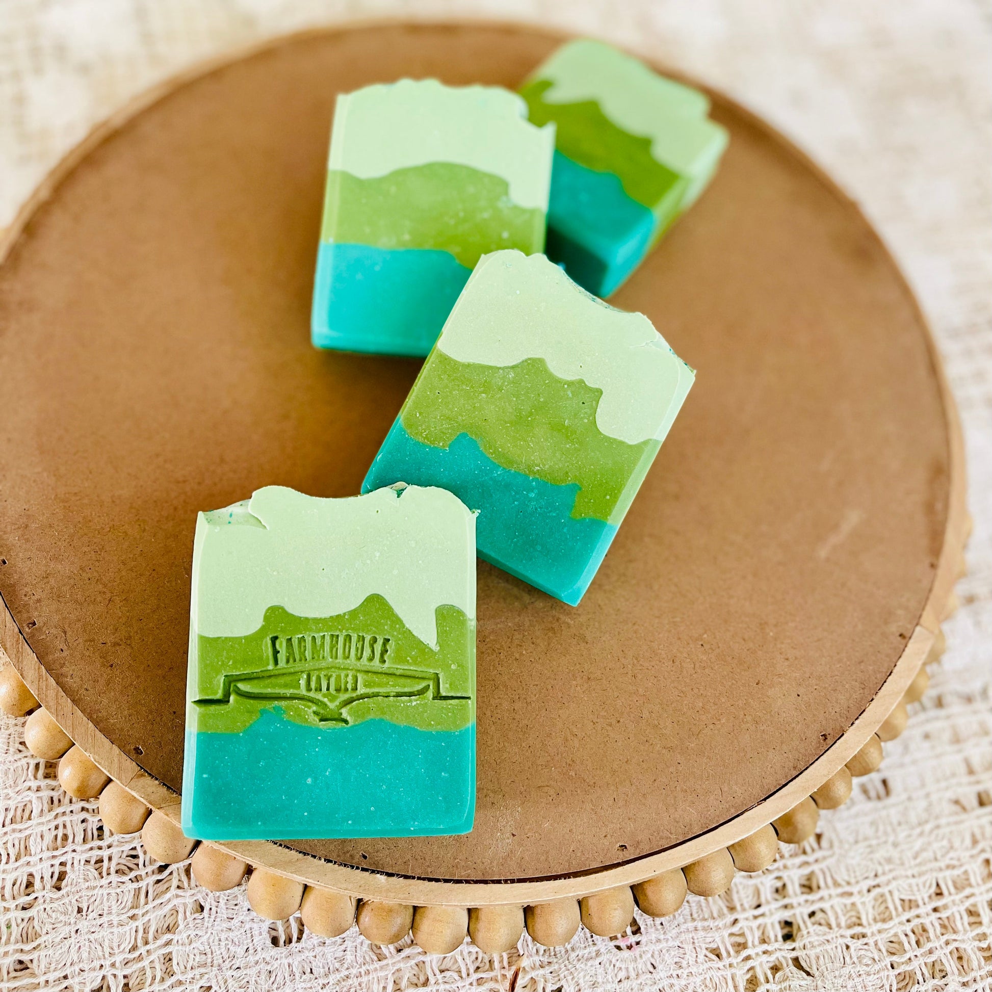 Green and teal soap bars with white tops, three pieces on round board
