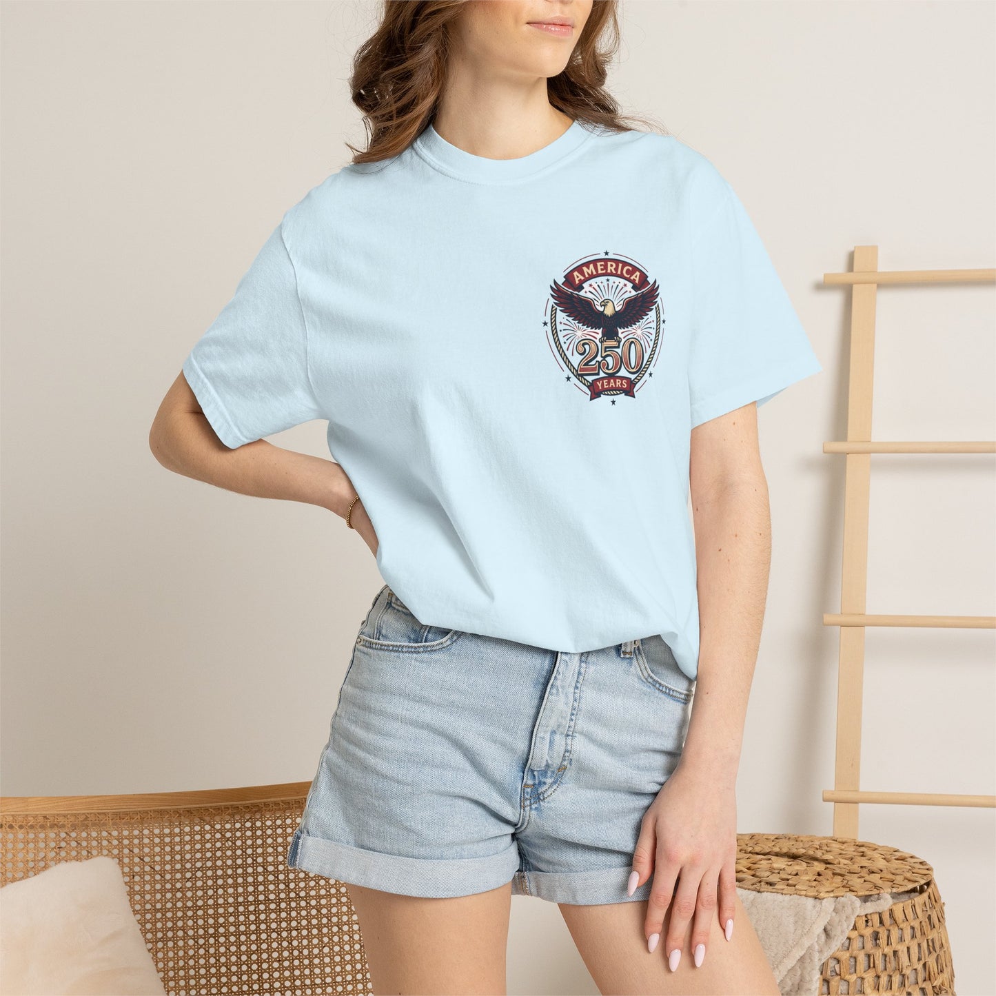 Light blue T-shirt worn by model, with round “America 250 Years” emblem on chest