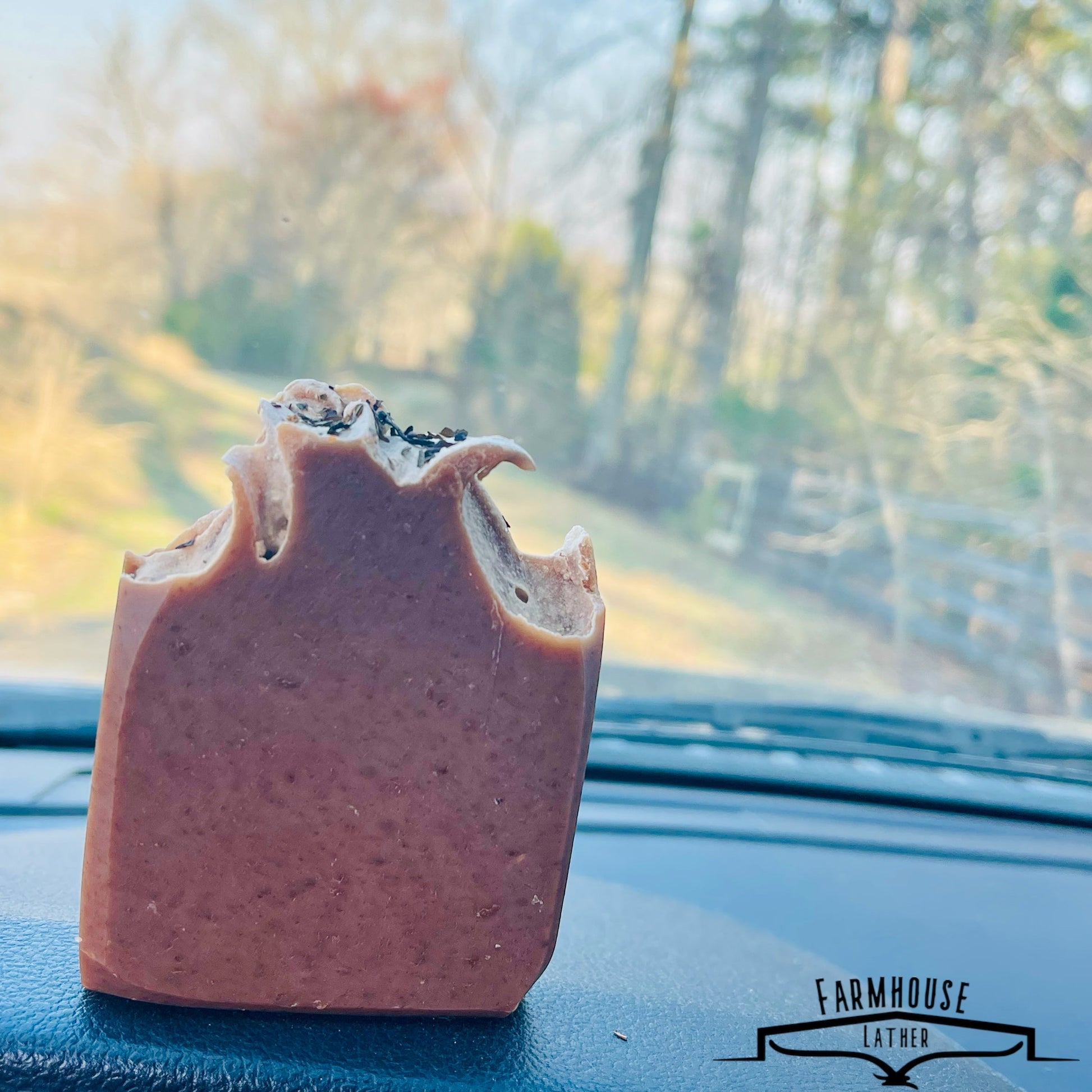 Bar soap in brown with herb flecks, angled view resting on dashboard surface