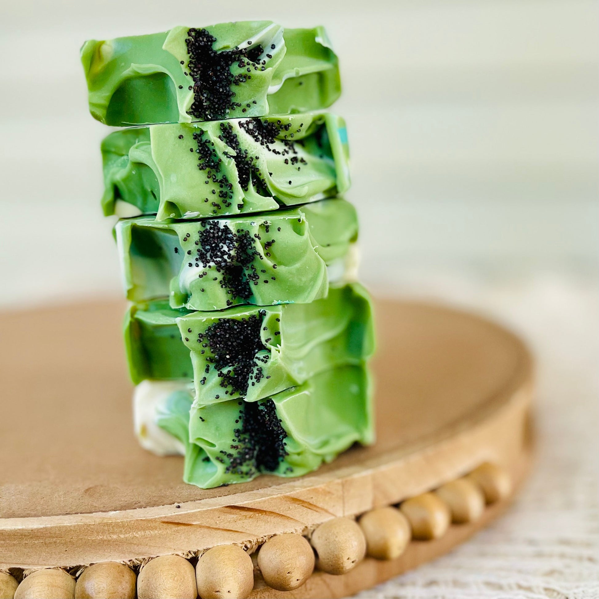 Stacked green soap bar with teal stripes and black speckles on a wooden tray.
