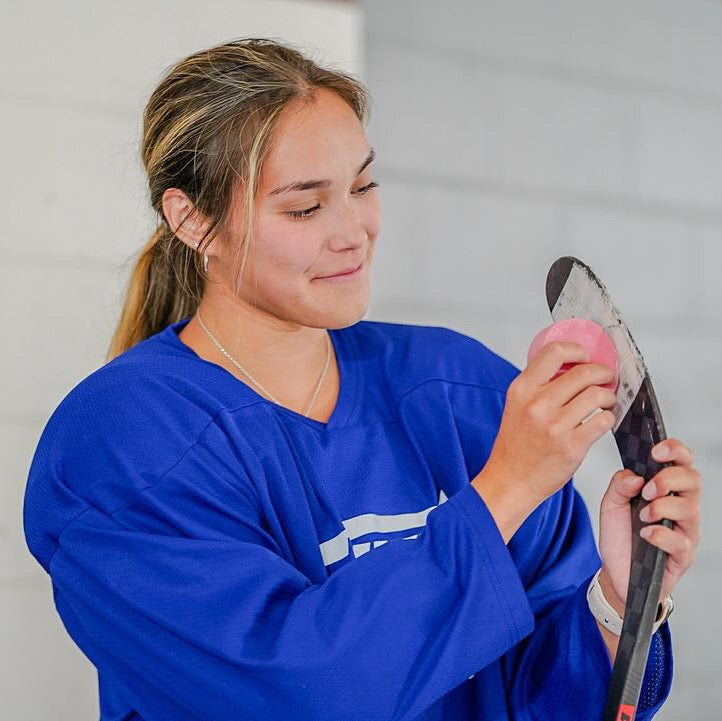 Female athlete holding a black hockey wax tin with pink wax on the lid
