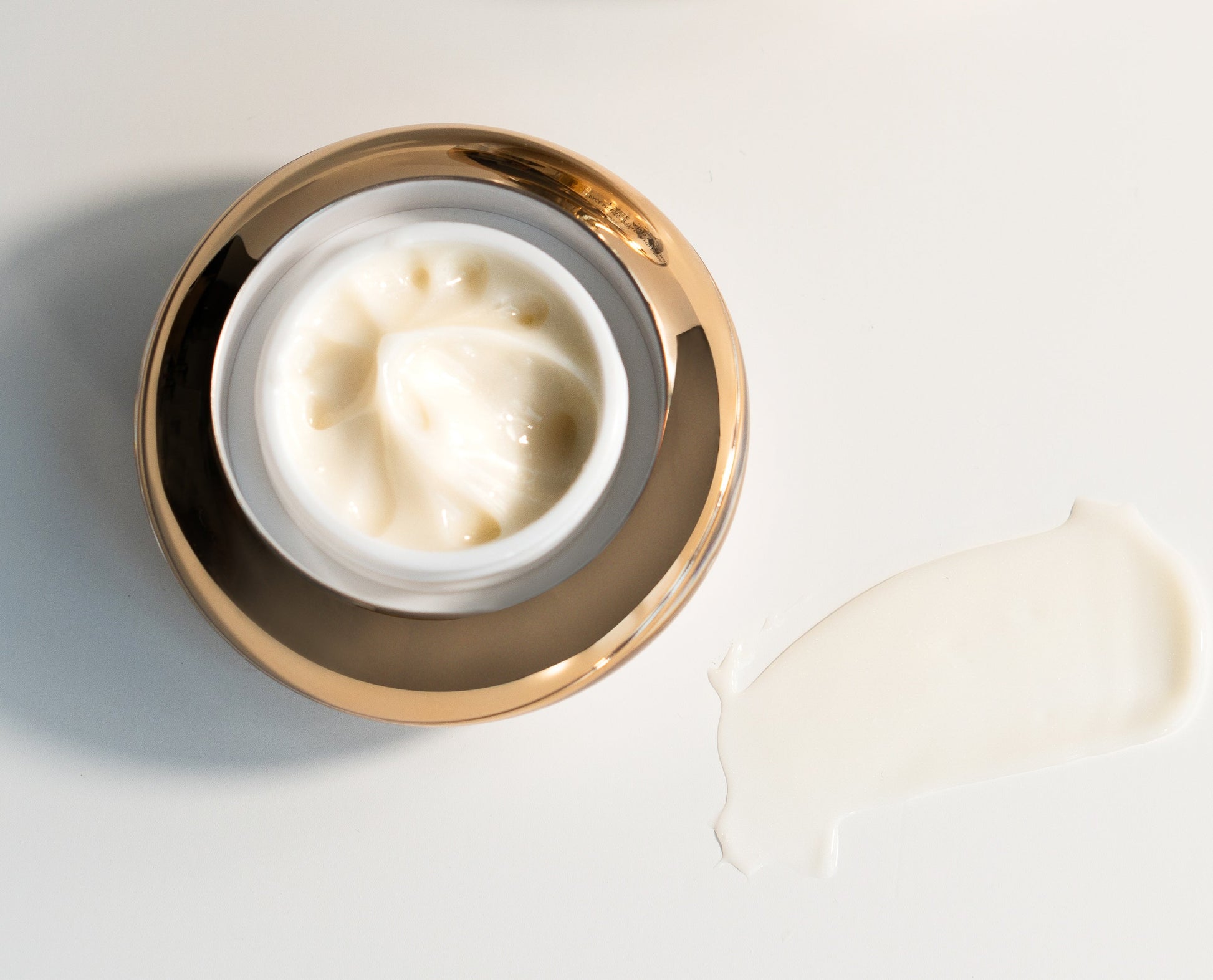 Under eye cream jar top view with thick white cream and gold rim.
