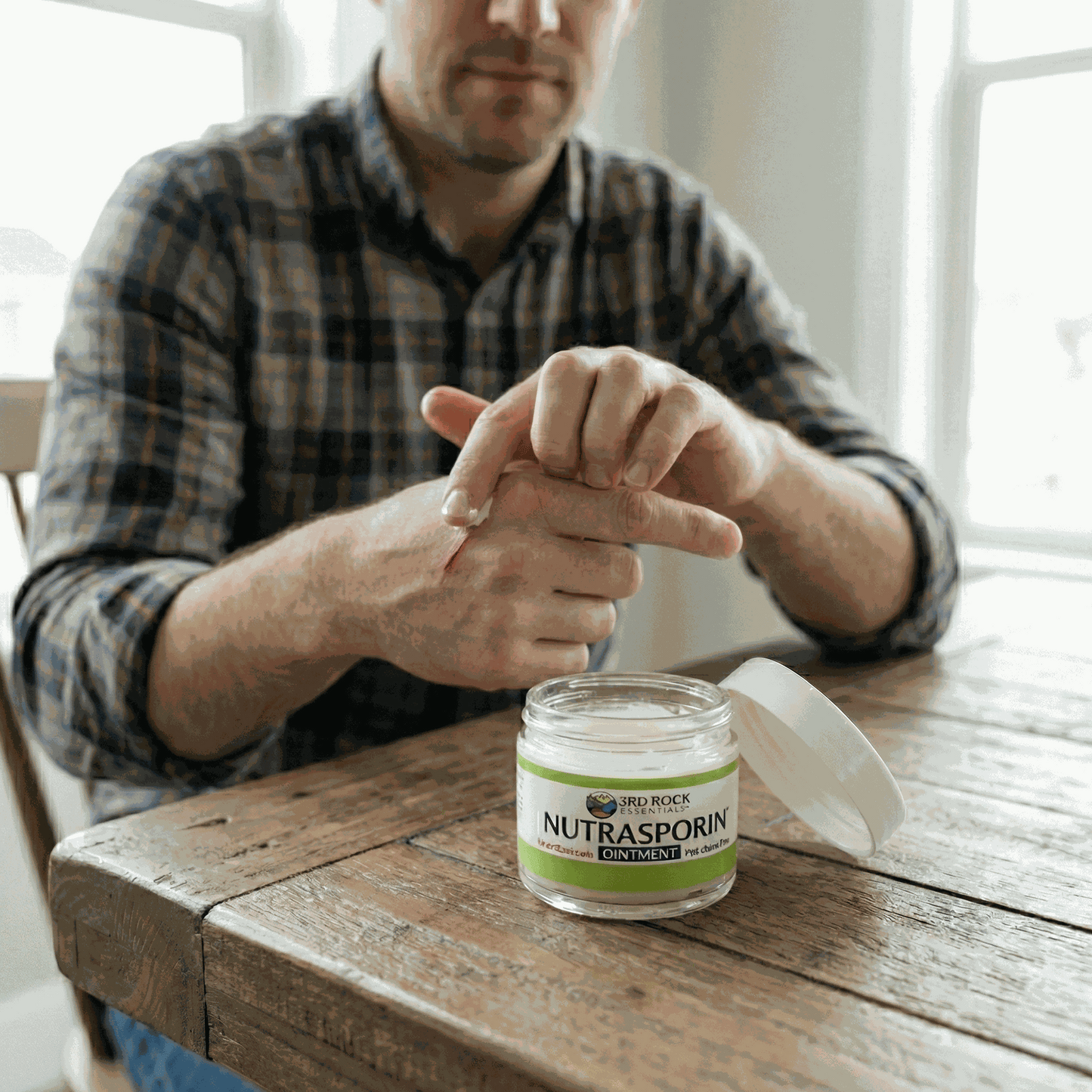 Nutrasporin ointment jar on wooden table while hands apply ointment to wrist