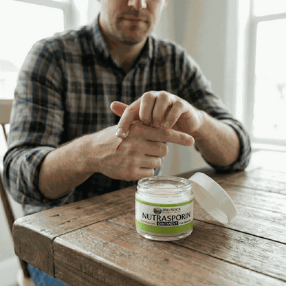 Nutrasporin ointment jar on wooden table while hands apply ointment to wrist