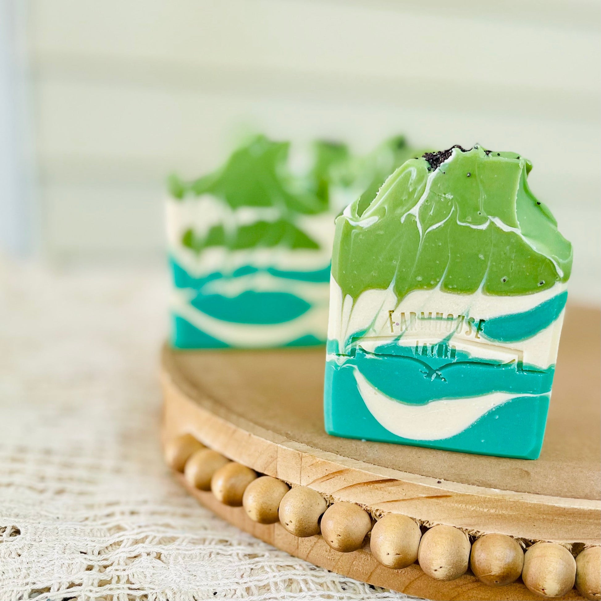 Layered green and teal soap bar on a wooden tray with bead edge.