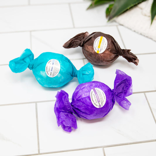 Bath bomb trio: blue, purple, and dark brown wrapped bombs with labels