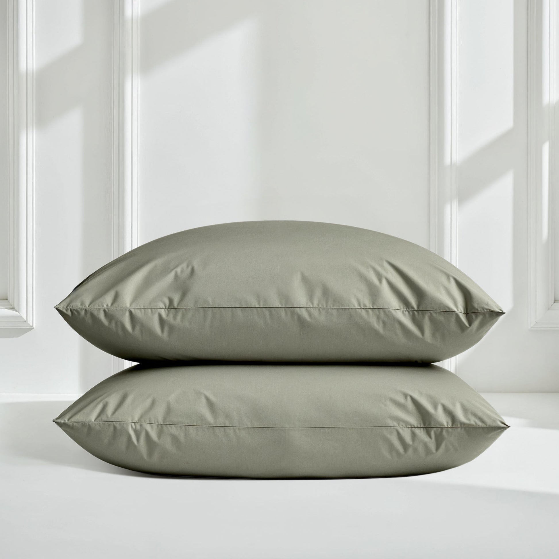 Sateen sheet set in moss green with two pillows stacked on bed