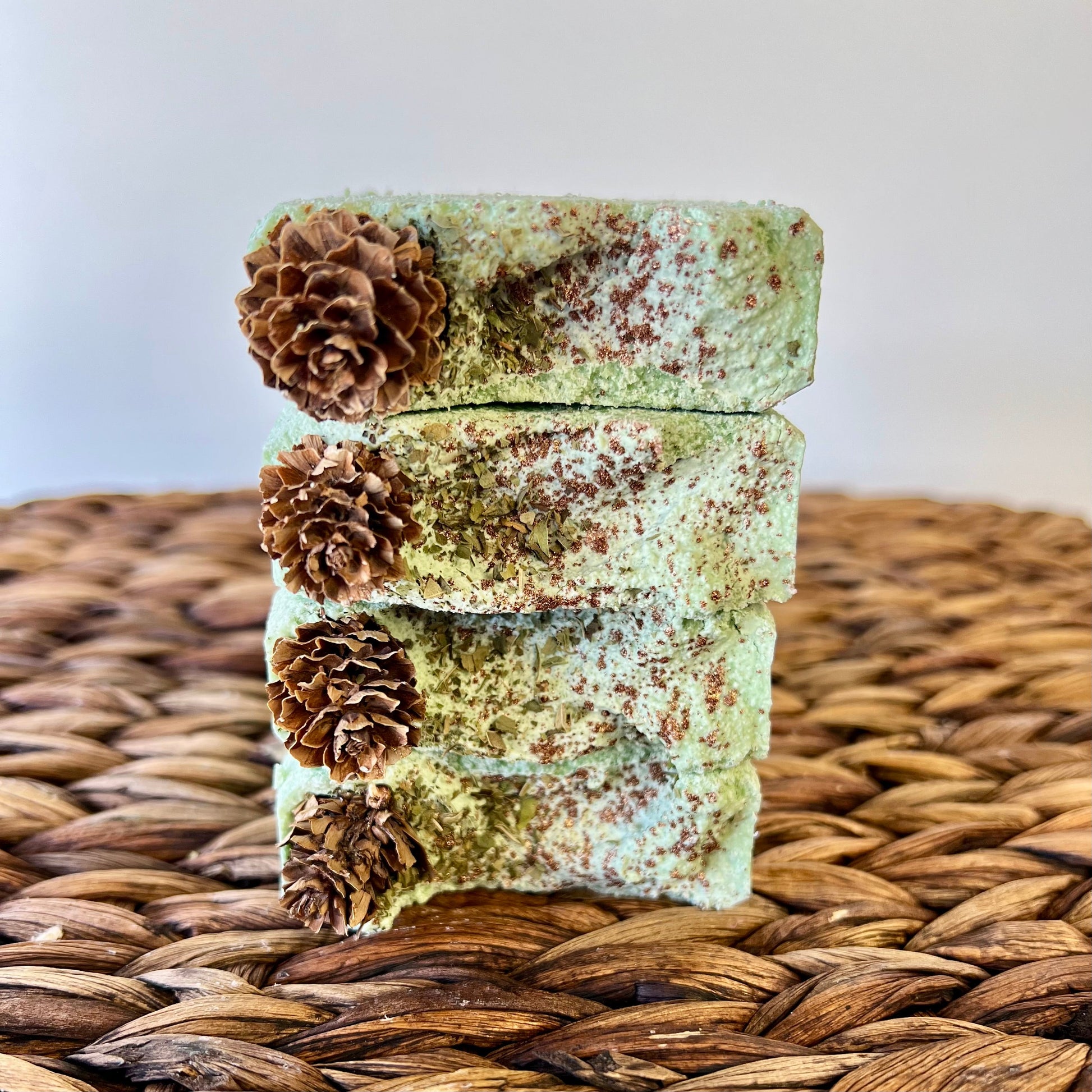 Stacked green sea salt soap bars with pinecone accents on woven mat