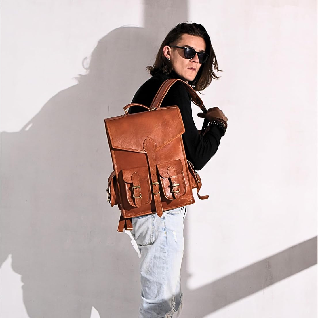 Brown leather backpack with flap and side buckles, worn on shoulder straps.
