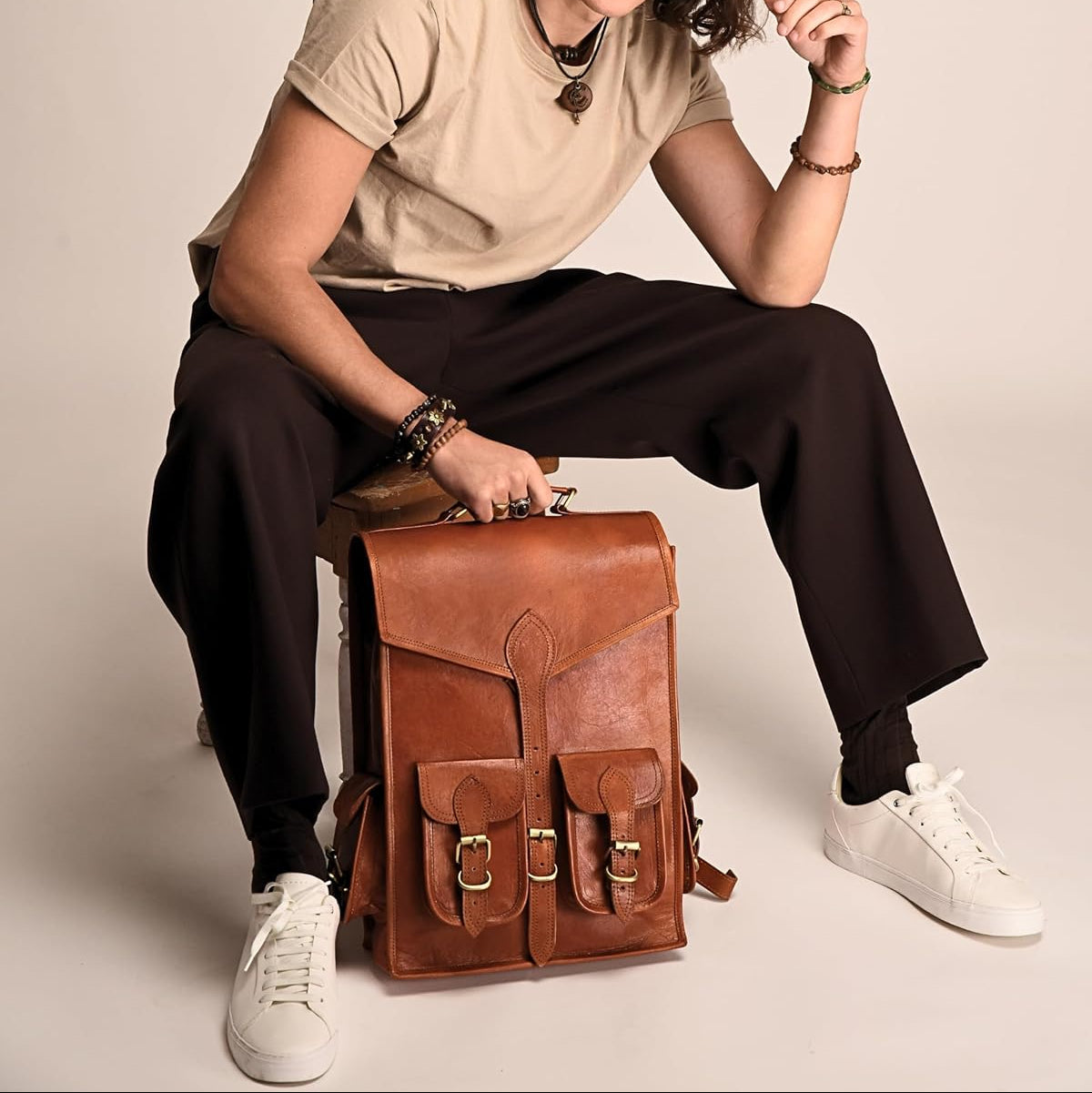 Brown leather backpack with front flap, two front pockets, and brass buckle details.