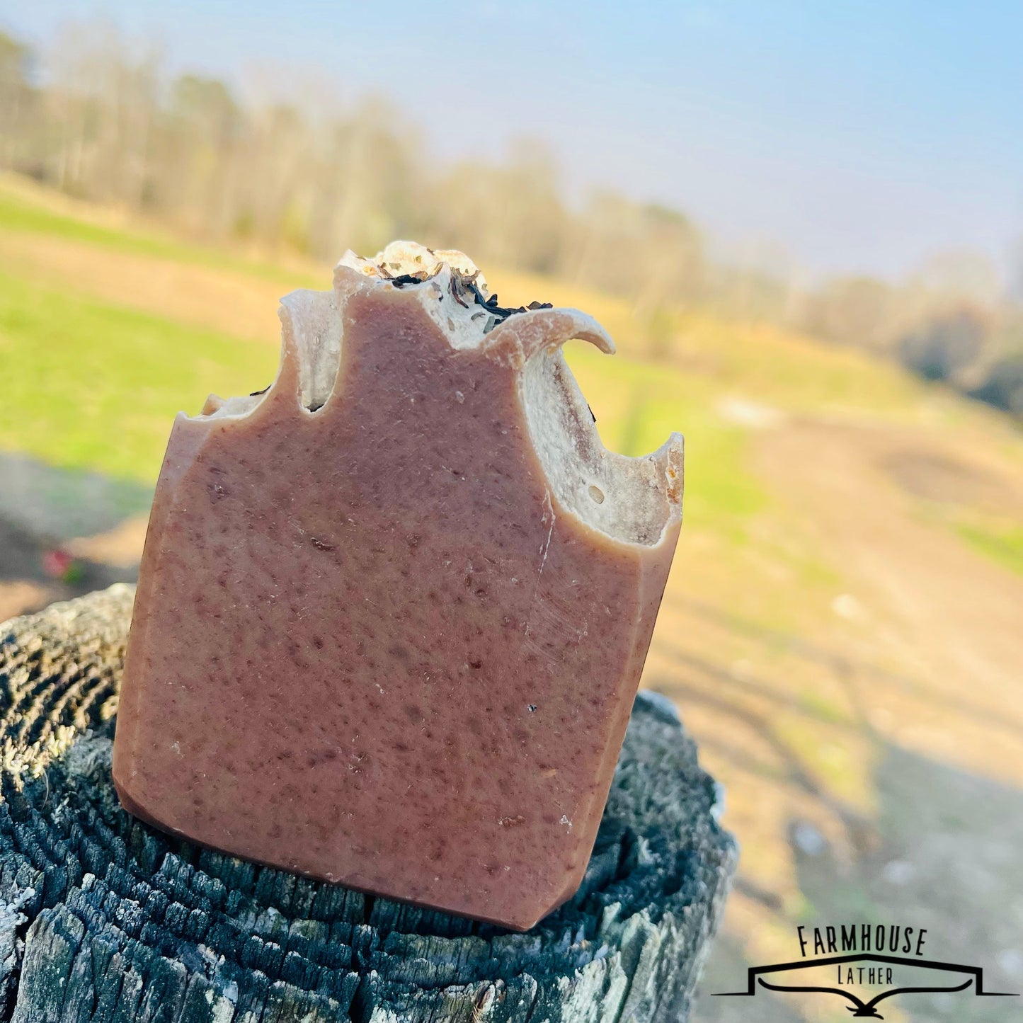 Bar soap with brown color and embedded herb flecks, upright on textured fabric