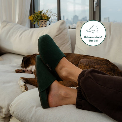 Forest green open-heel house slippers on sofa, slip-on style with FULTON logo.