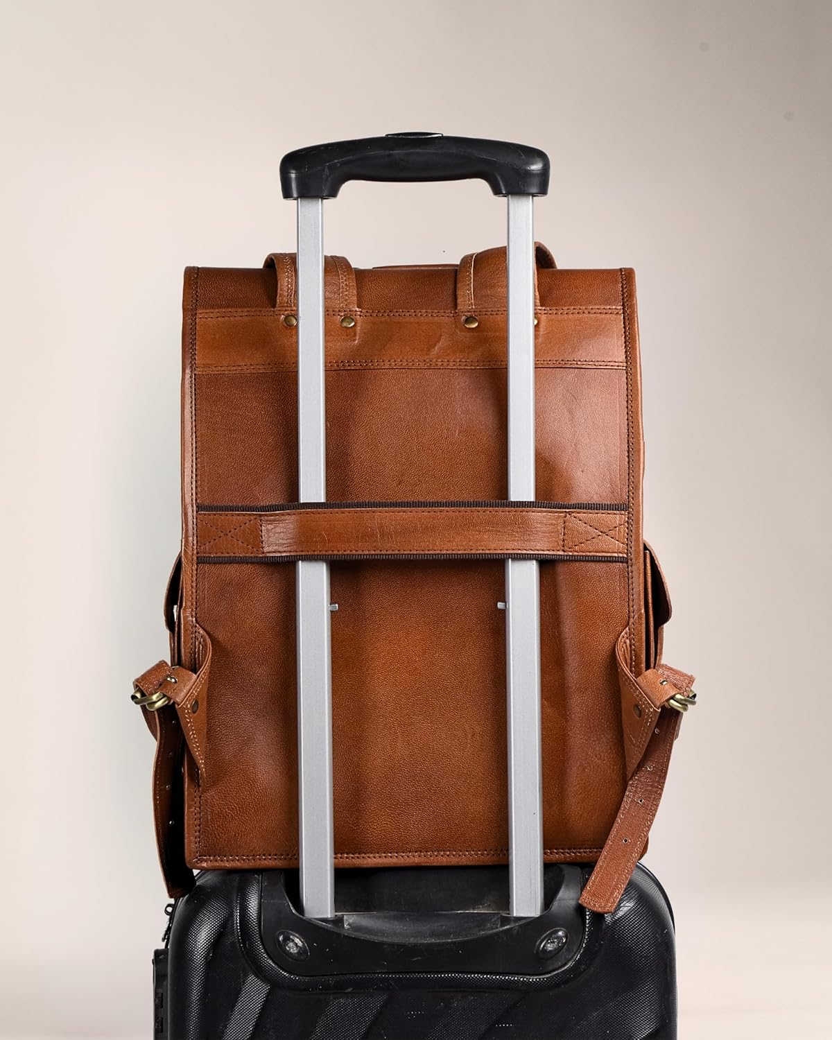 Brown leather backpack with black trolley sleeve and reinforced pick-up handle, rear view.