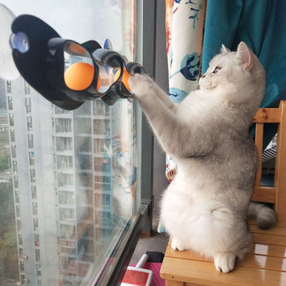 Grey cat track toy on suction cups with orange ball ports, held up by a climbing cat