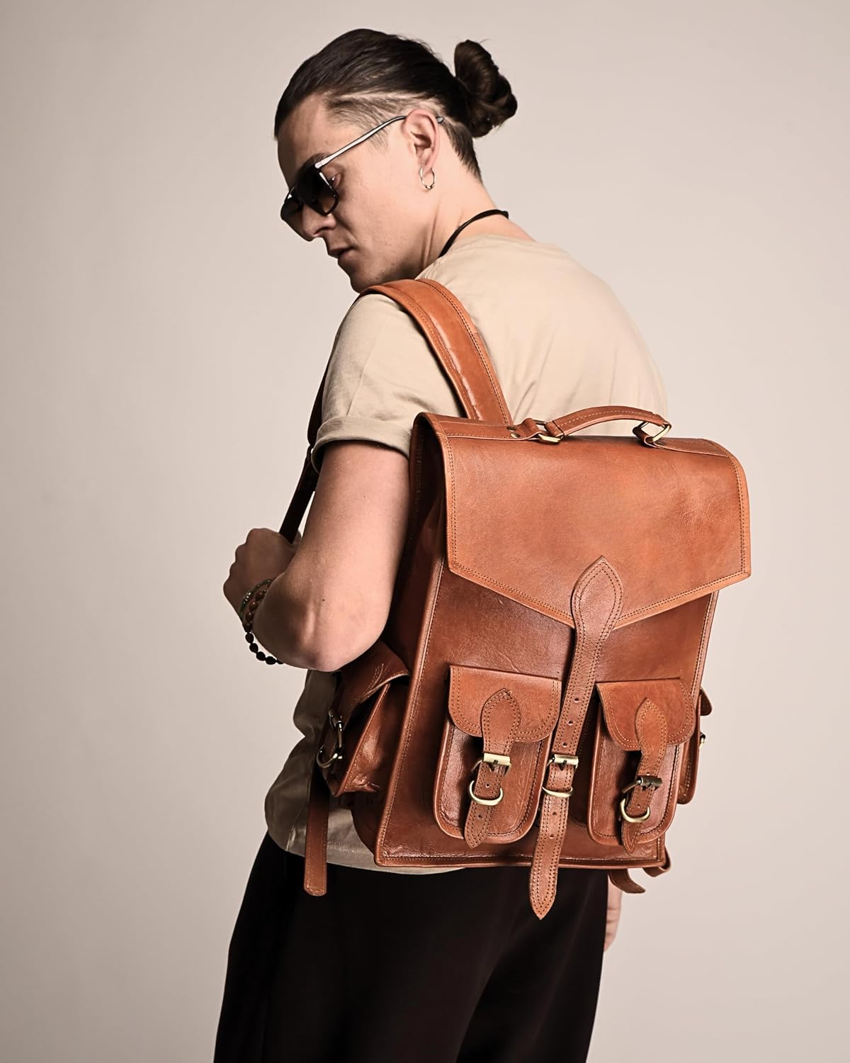 Brown leather backpack with flap and reinforced side straps, shown from the side.