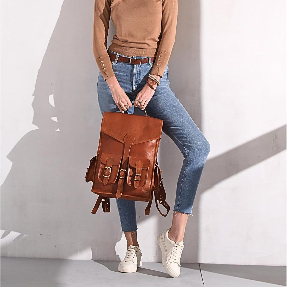 Brown leather backpack with flap top and front strap pockets, carried at the side.