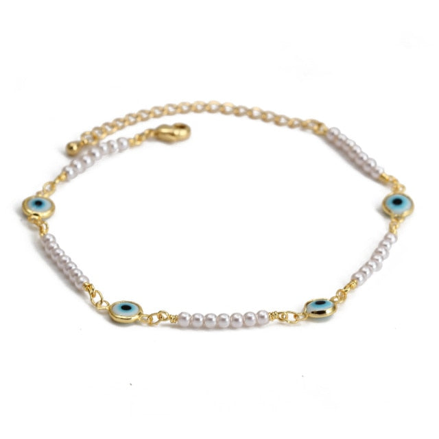 Charm bracelet with gold chain, white beads, and blue evil-eye charms