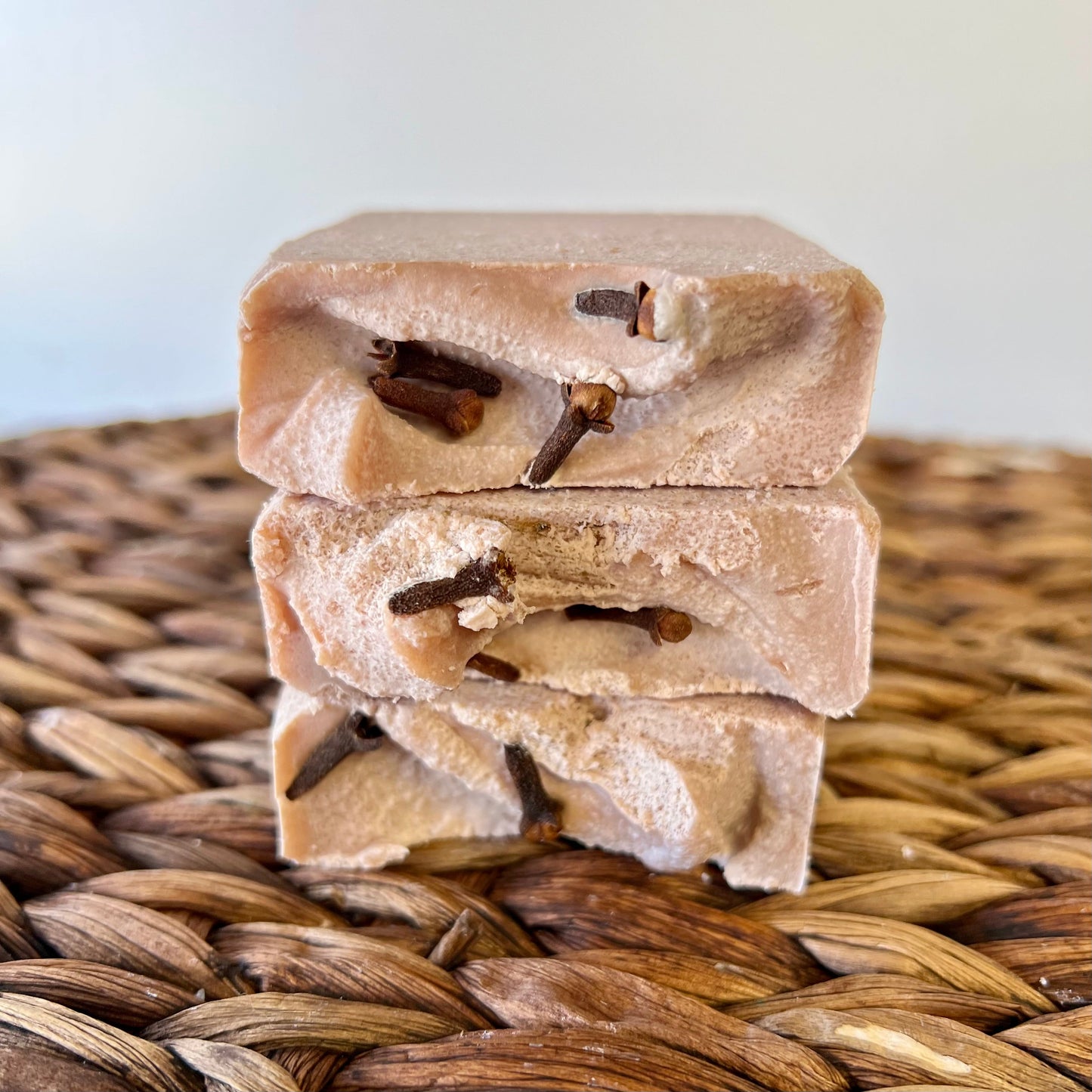 Stacked beige soap bars with dark embedded pieces, viewed from the side on mat.