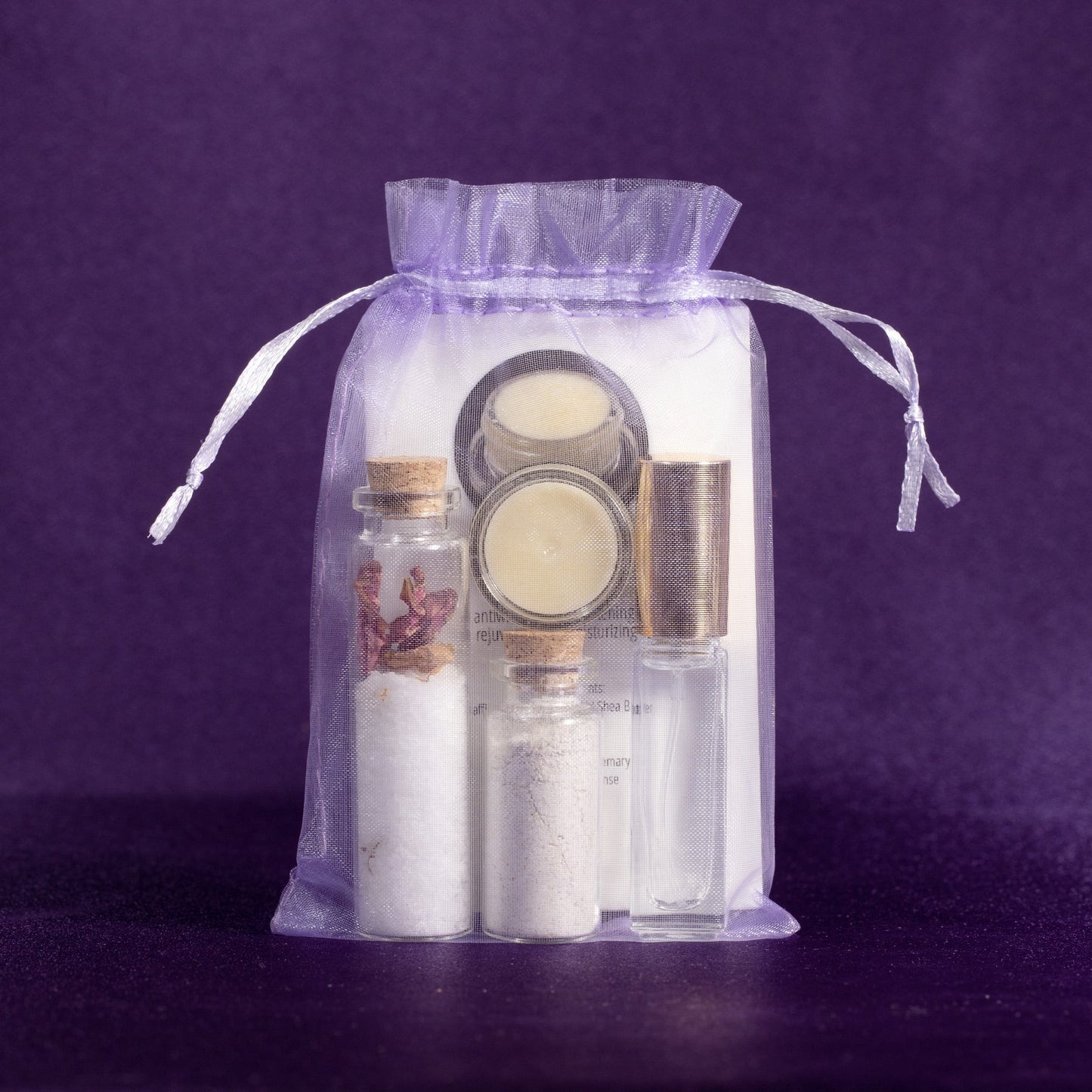 Clear drawstring gift pouch containing glass bottles, salt jars, and cream in jars