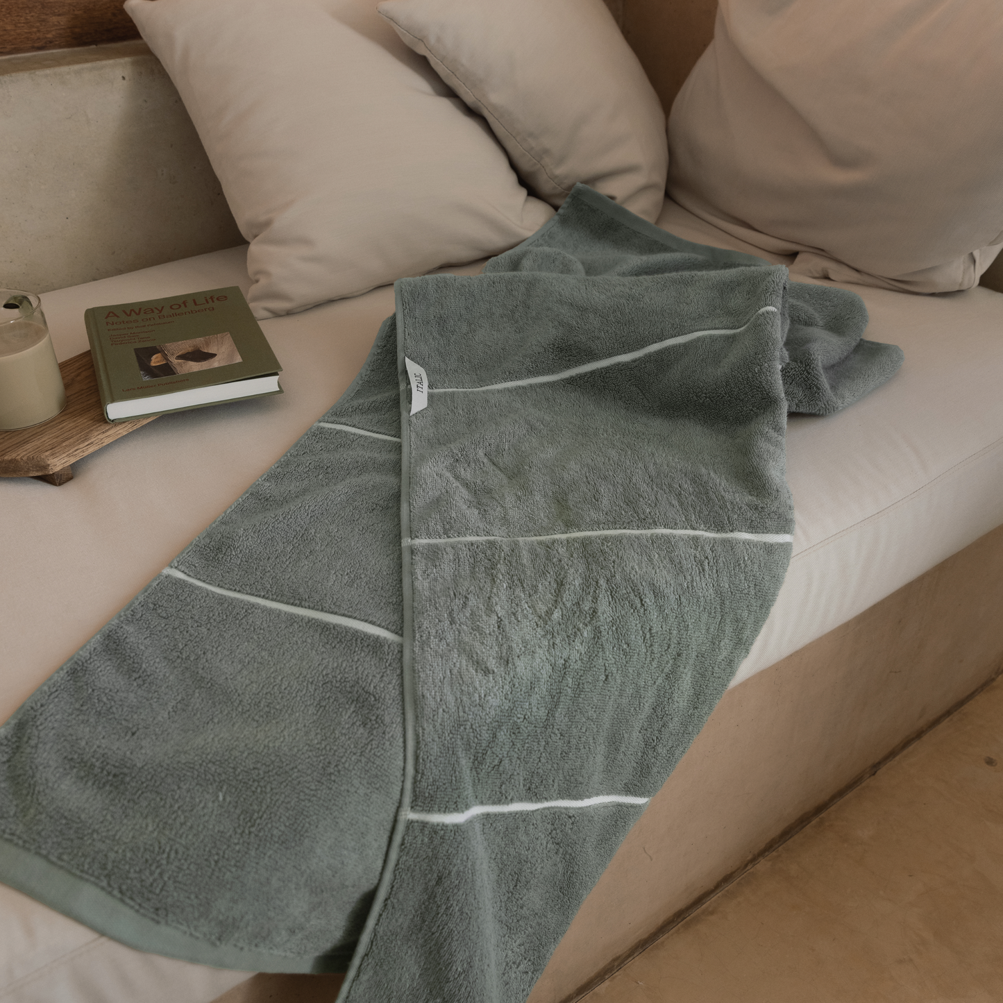 Sage green cotton towels with white border lines, folded and draped on couch