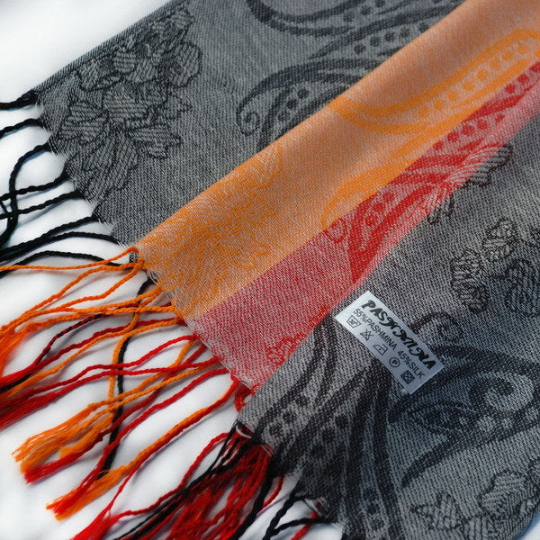 Gray paisley pashmina scarf close-up with orange and red stripe band and black fringe