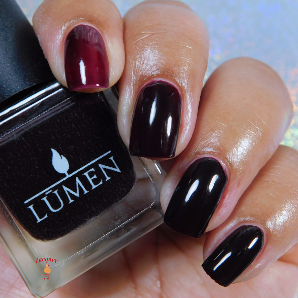 Burgundy and dark glossy fingernails with nail polish bottle edge visible