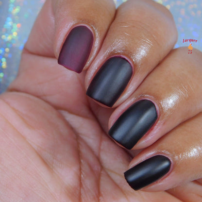 Dark matte fingernails with nail polish bottle partially visible