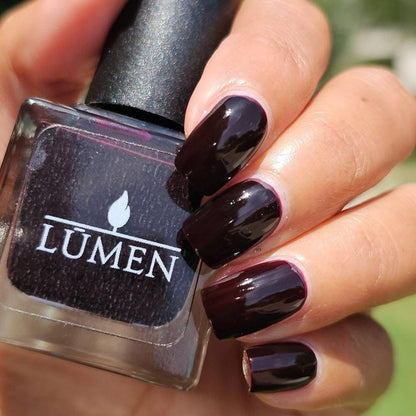 Nail polish bottle labeled LUMEN with deep burgundy glossy fingernails