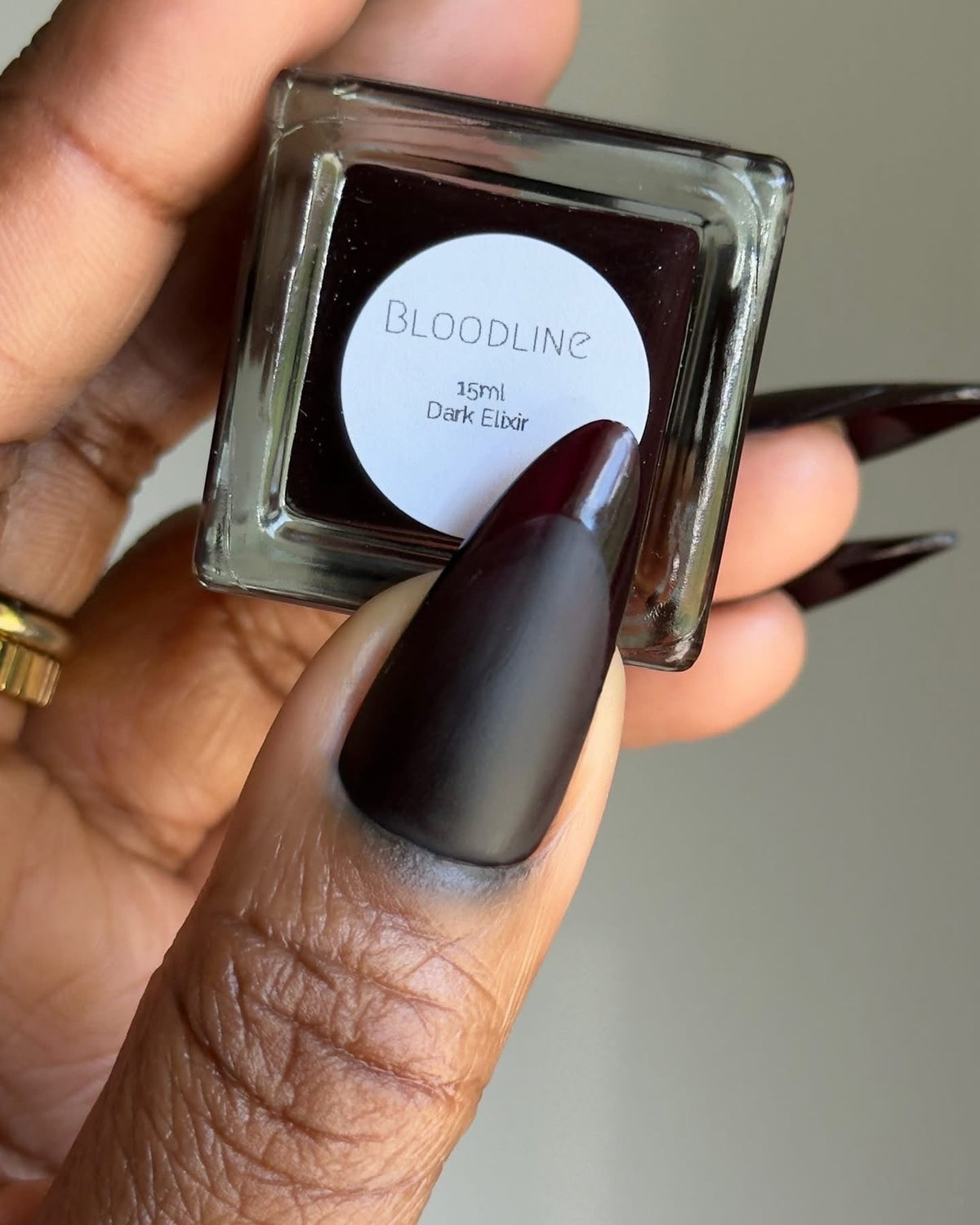 Nail polish bottle labeled Bloodline, 15ml, dark elixir, with dark nails