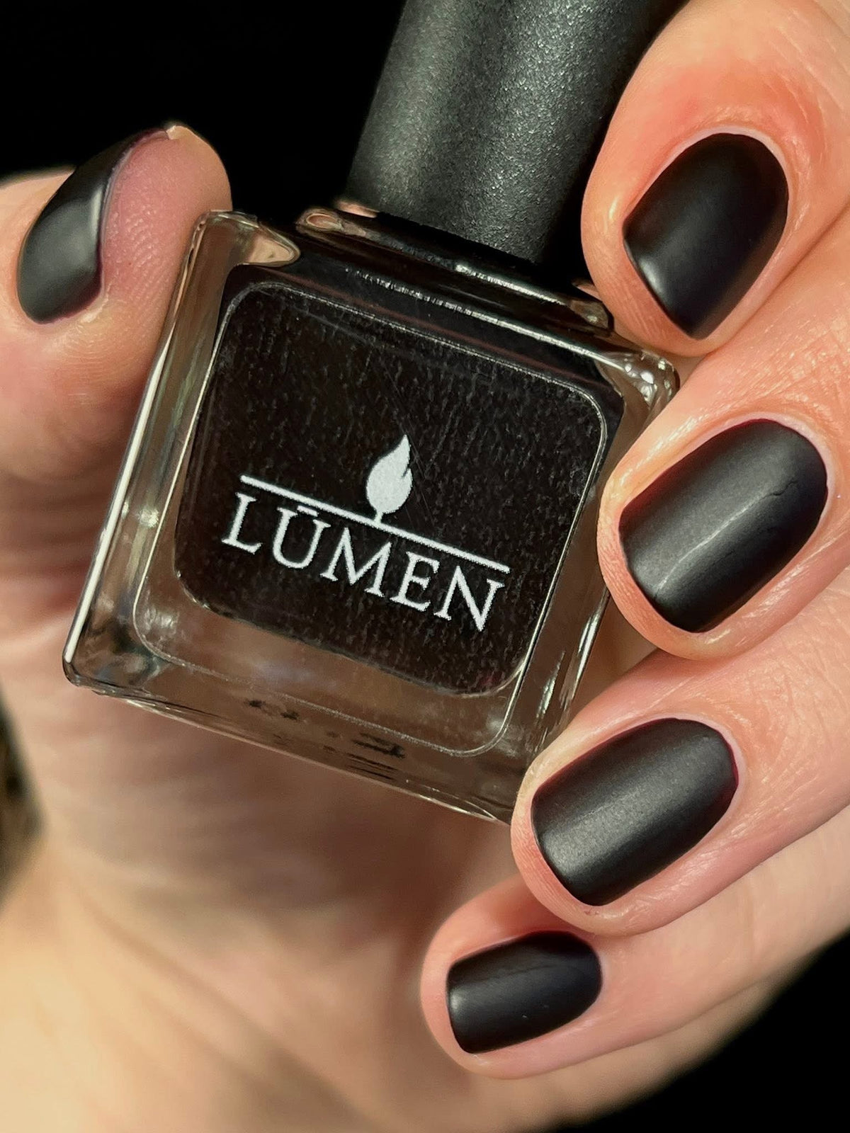 Nail polish bottle with LUMEN label; matte dark nail polish on fingers