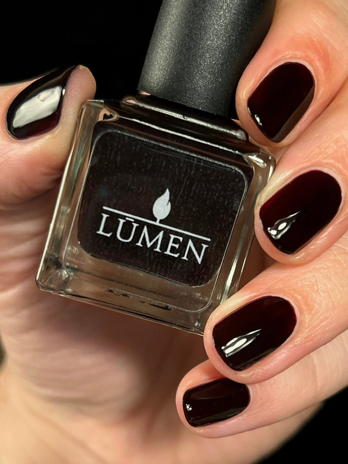 Nail polish bottle with LUMEN label; dark matte nails with one glossy accent