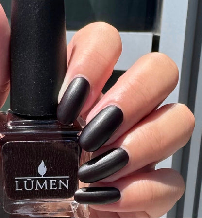 Nail polish bottle beside hand; matte dark oval nails