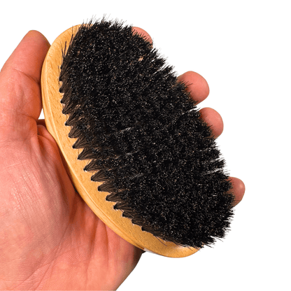 Wood boar bristle hair brush with black bristle side held in hand