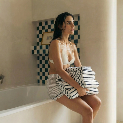 Striped cotton towels stack, white with navy bands beside bathtub