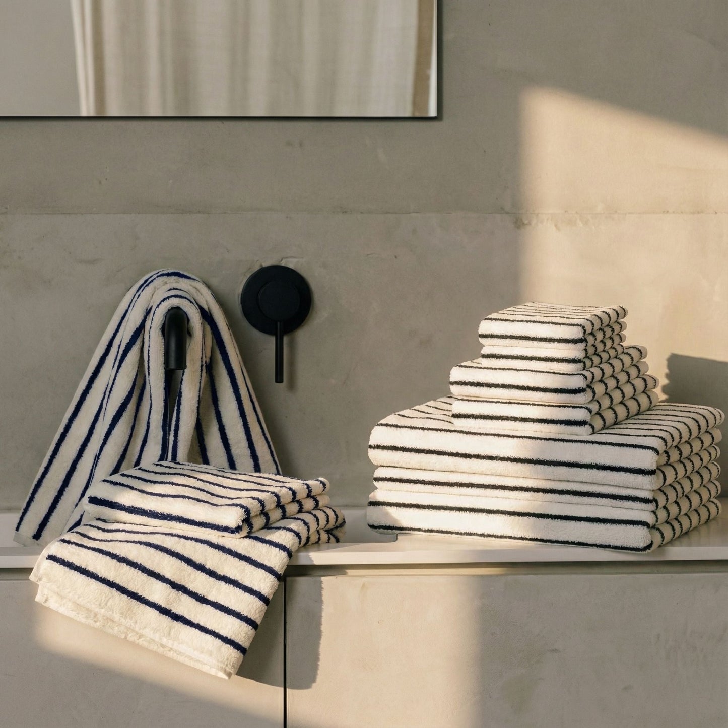 Plush cotton towels, white with navy stripes, stacked on a wall shelf