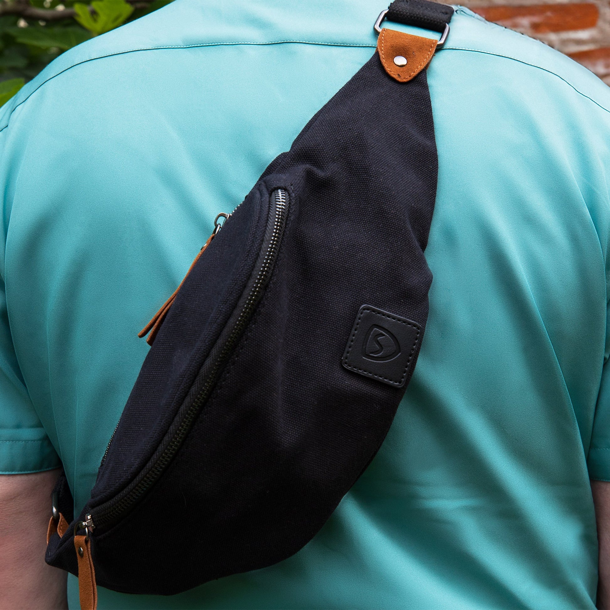 Canvas crossbody fanny pack, black with tan leather trim; worn on torso