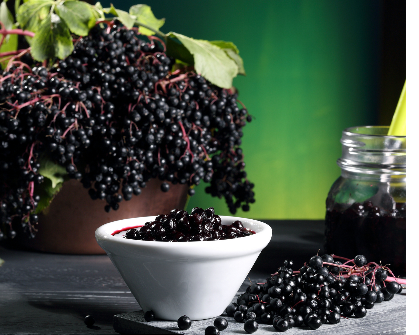 Elderberries in a white bowl with small jar, green background