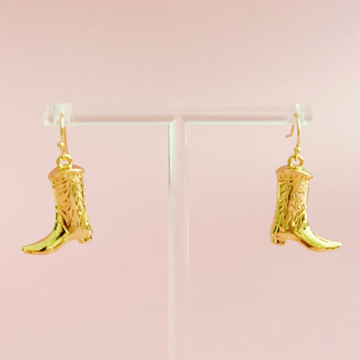 Gold-tone cowgirl boot dangle earrings hanging from a clear display