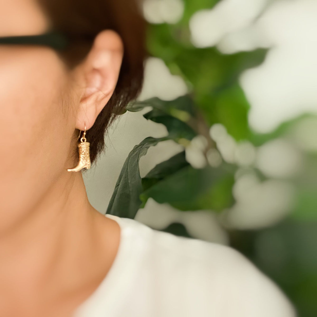 Gold-tone cowgirl boot dangle earrings worn on the ear
