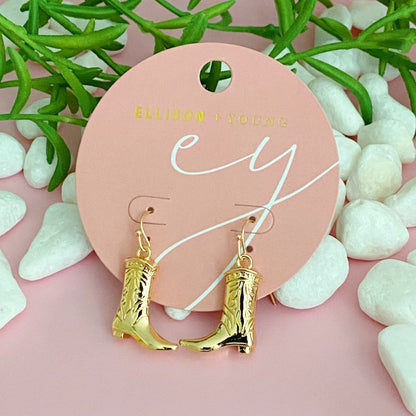 Gold-tone cowgirl boot dangle earrings on a pink retail card