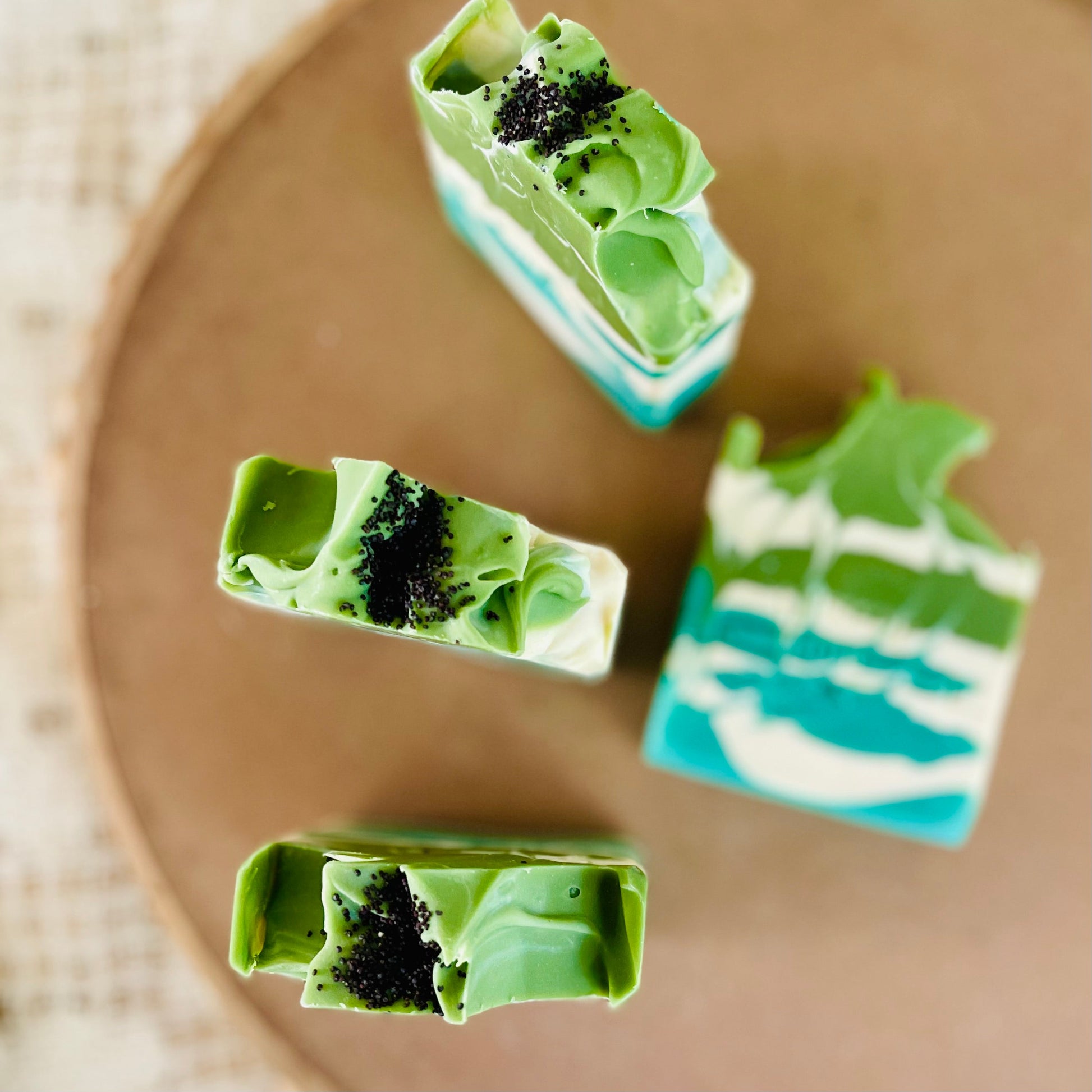Assorted green soap bars with teal layers and black speckles on a circular board.